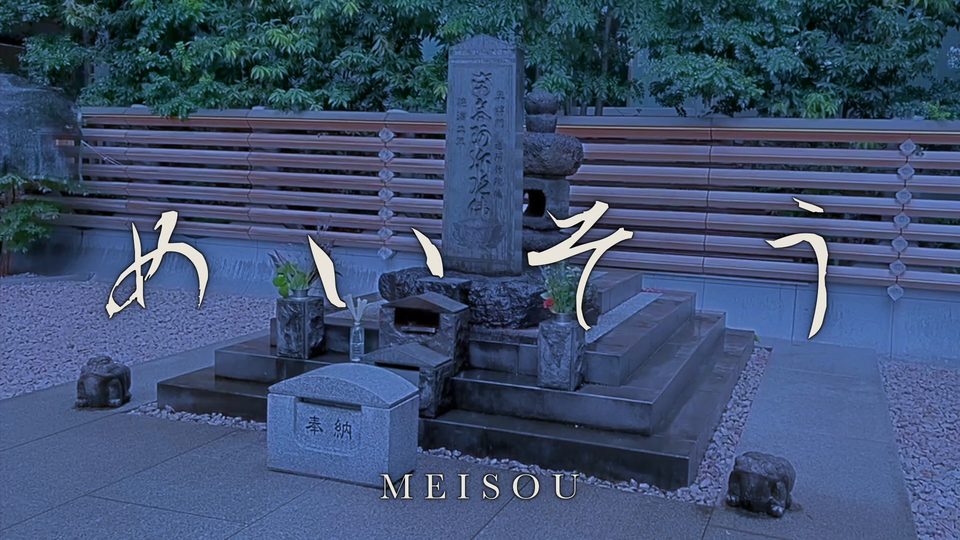 The title めいそう in white brush lettering over a gray-blue stone memorial in Tokyo.
