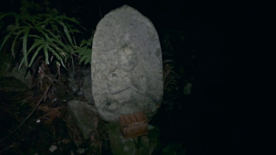 A weathered stone Buddha in the dark, lit only by a headlamp.