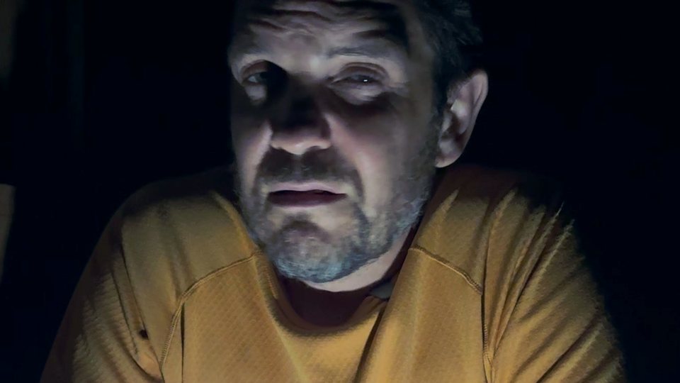 Night in a mountain hut: the hiker, lit from below, whispers a story into the camera.